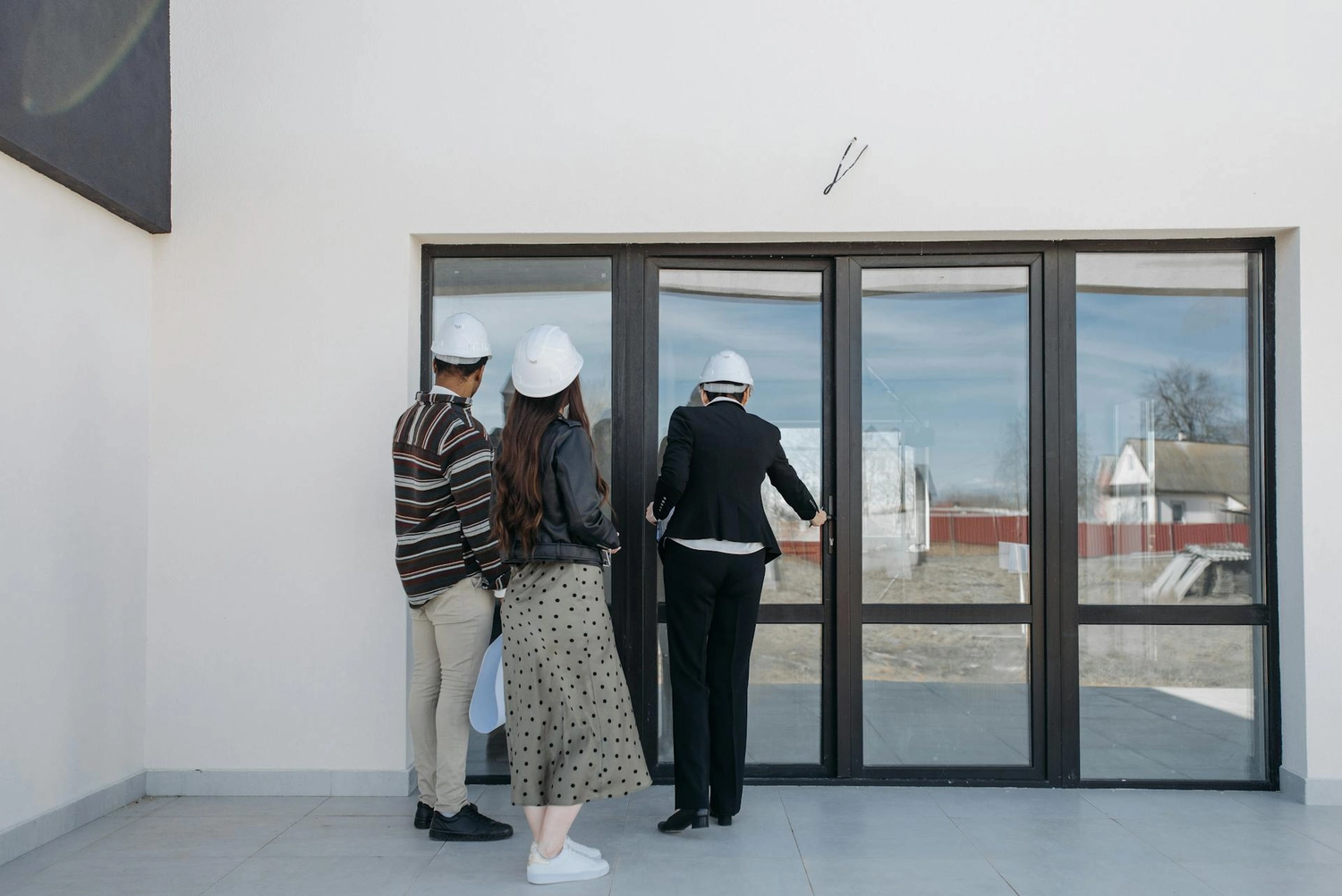 Roland Renner GmbH - Immobilienverwaltung und Gebäudedienstleistungen - Drei Personen mit Schutzhelmen stehen vor einem modernen Gebäude mit großen Glasfenstern.